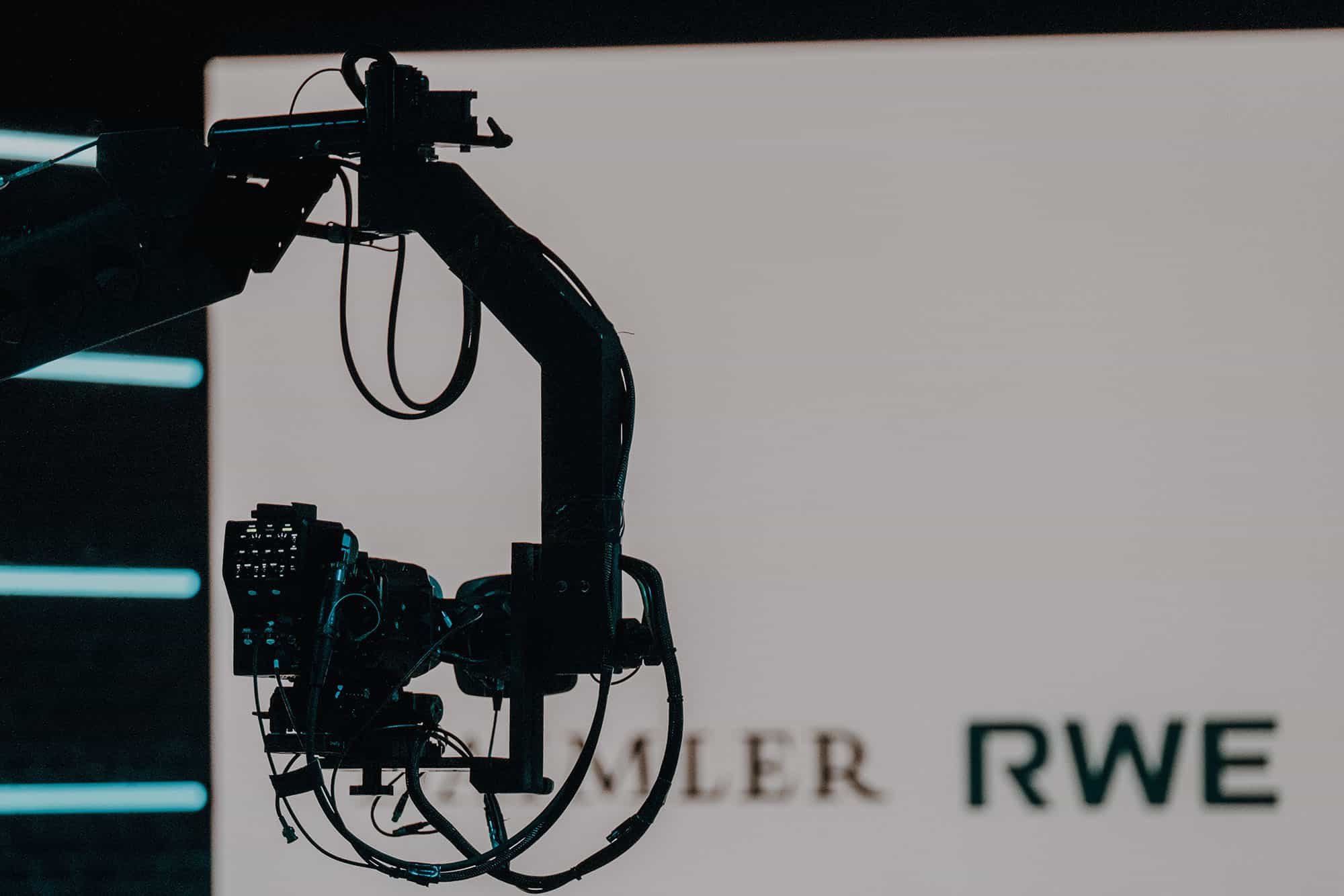 Im Vordergrund ist ein Kamerakran zu sehen, im Hintergrund mehrere Logos auf einer LED-Wand.